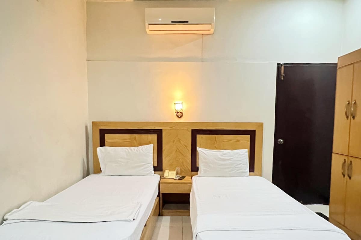 Una habitación de hotel con dos camas individuales, una mesita de noche con teléfono y lámpara, un armario y un aire acondicionado instalado en el techo.