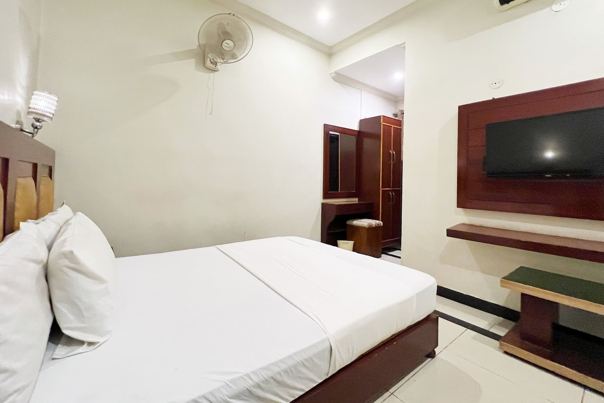 Una habitación de hotel con una cama, un televisor montado en la pared, un armario y un ventilador de techo.