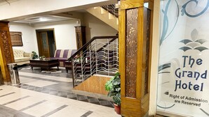 Una hall d'albergo con pavimento a scacchi, una scala con ringhiera decorativa e un cartello che indica il nome dell'hotel.