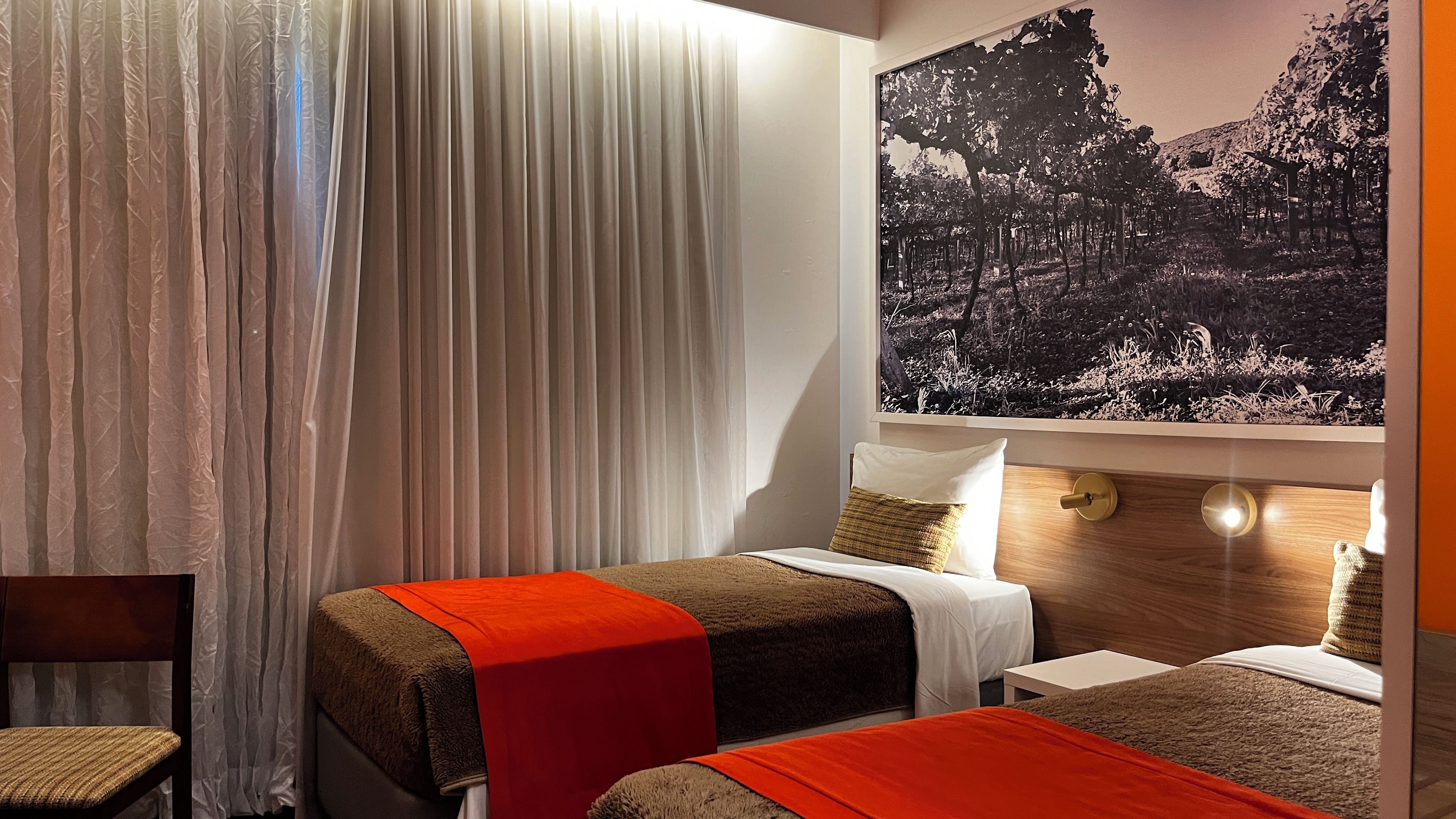 A hotel room with two beds, a large window with a forest view, and a curtain.