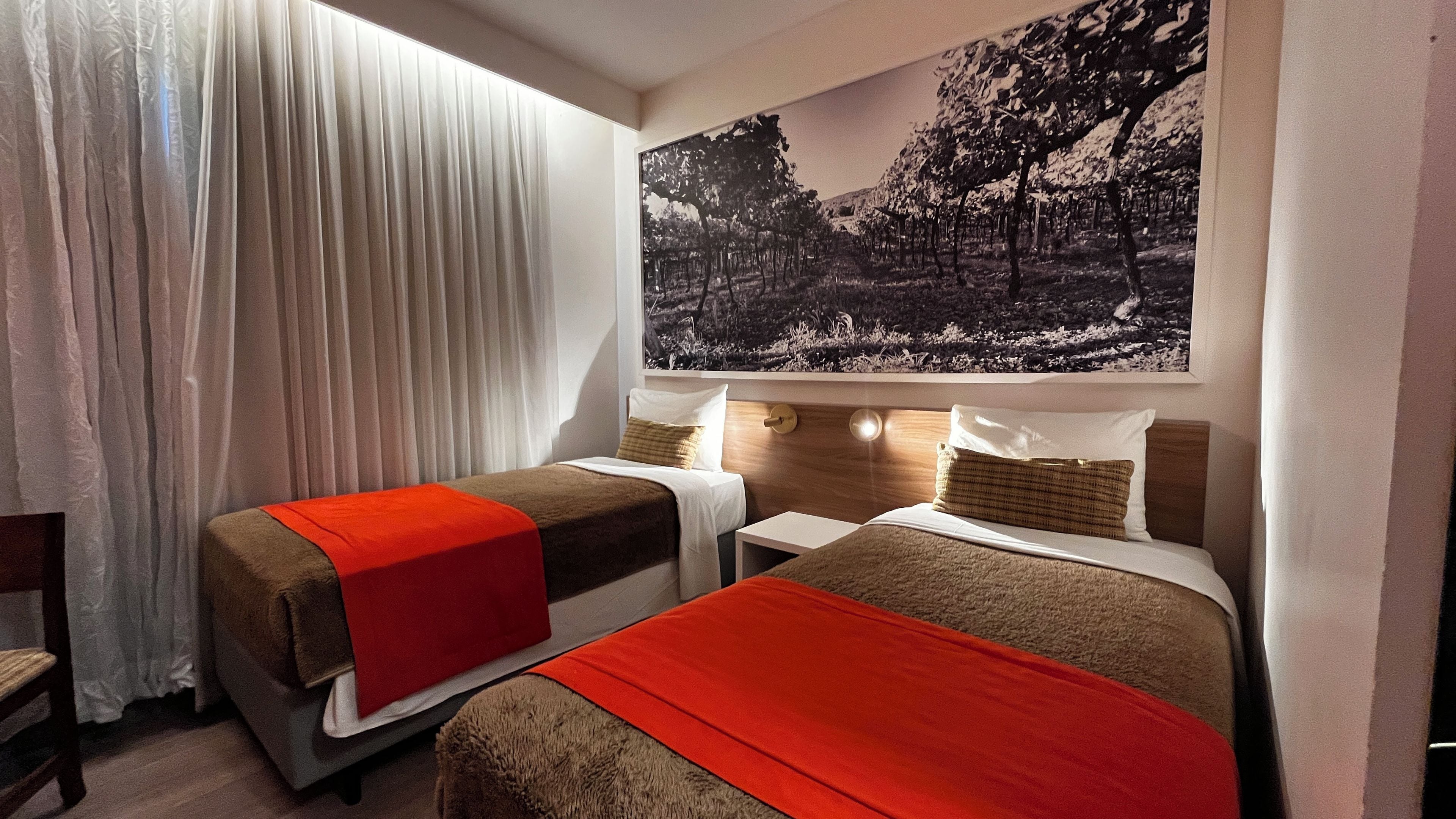 Una habitación de hotel con dos camas, un ventanal con cortinas y un cuadro colgado en la pared.