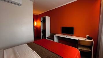Quarto de hotel com cama, escrivaninha, televisão, cadeira e guarda-roupa.
