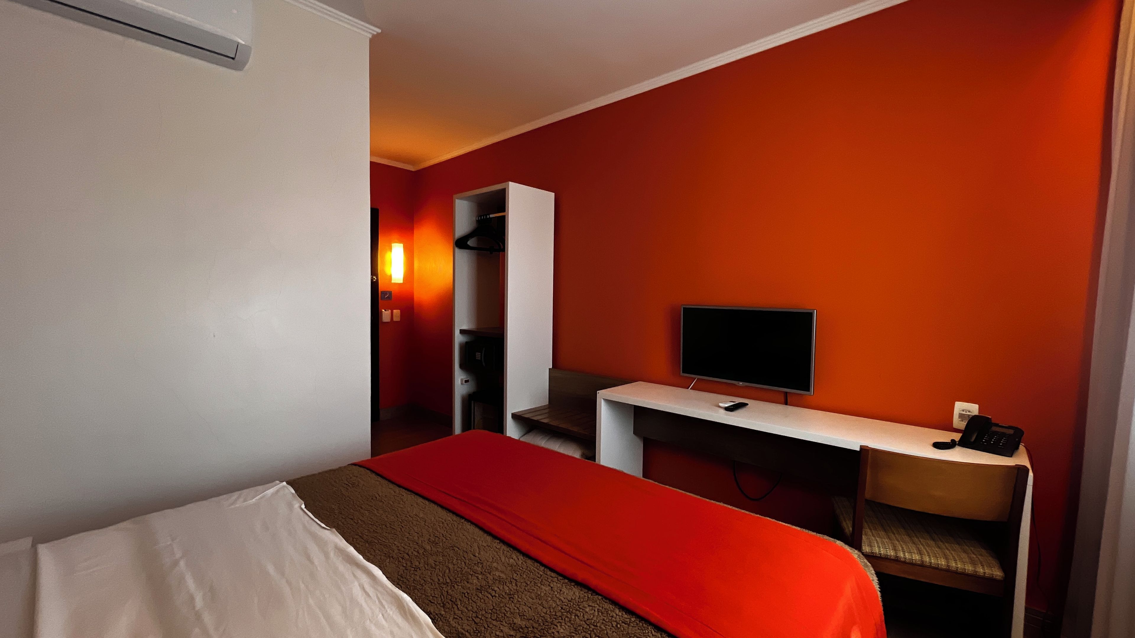 A hotel room with a bed, a desk, a television, and a telephone.