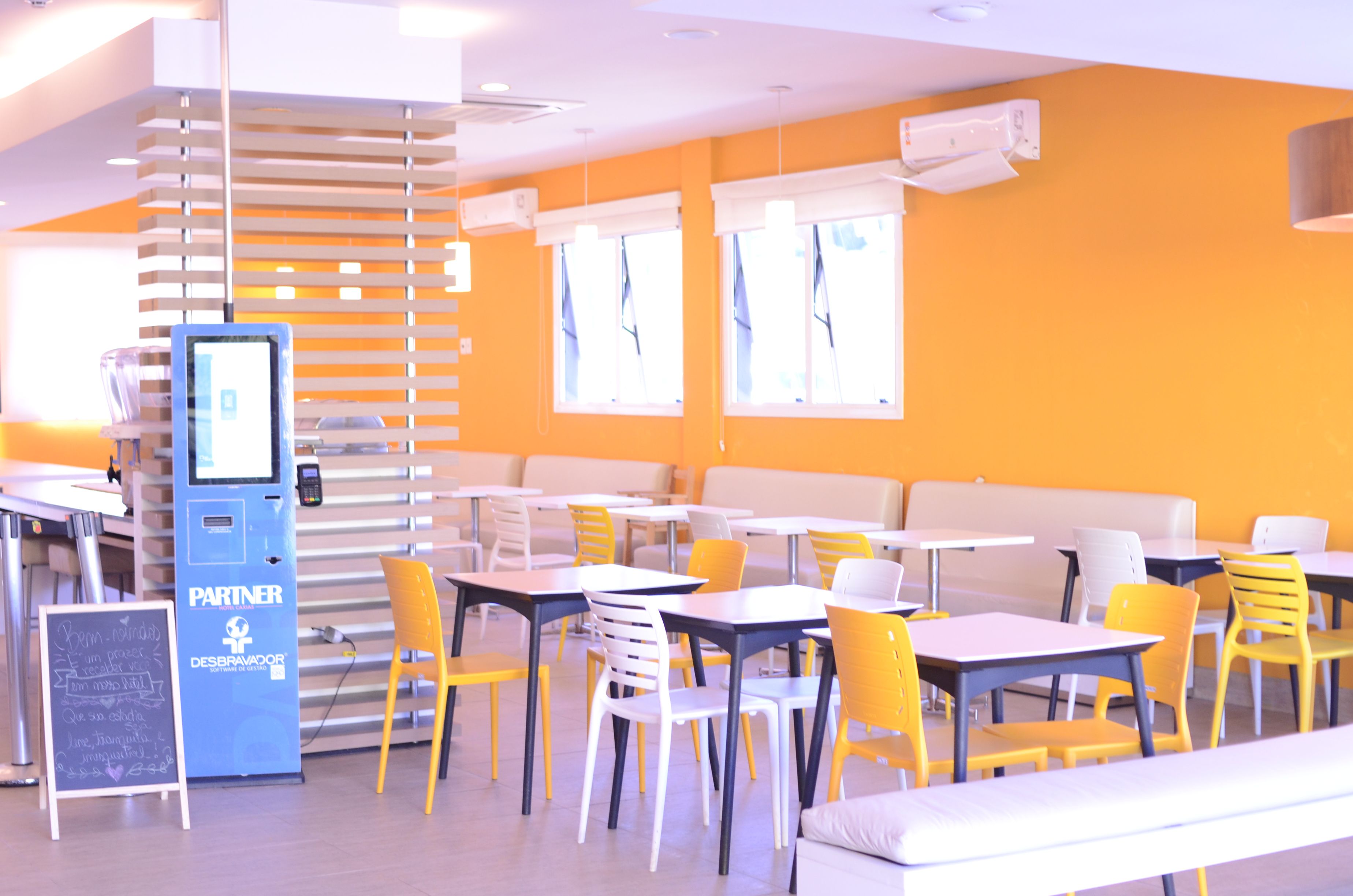 Zona pranzo moderna con tavoli e sedie, un chiosco self-service e una lavagna.
