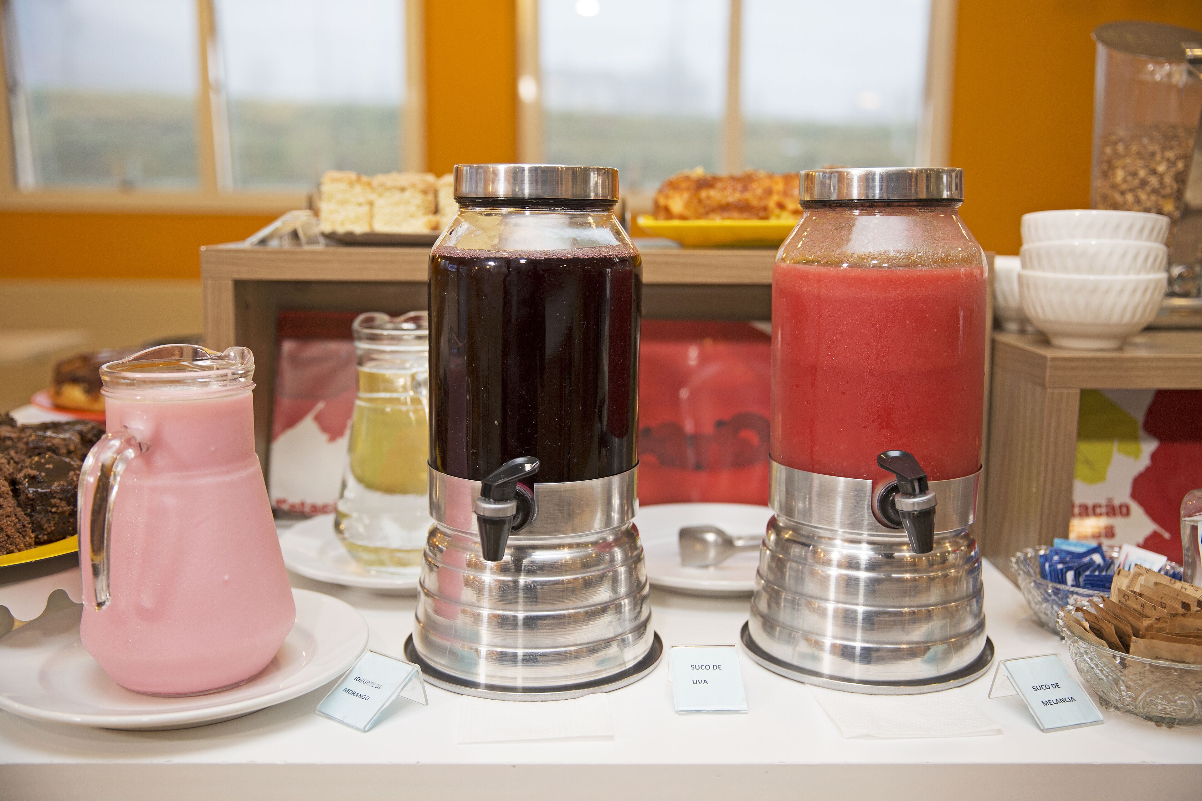 A beverage station with three dispensers, a plate of brownies, and a bowl of cookies.