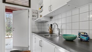 Et moderne køkken med hvide skabe, en stålvask og et flisebeklædt bagpanel.