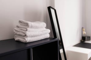 A stack of white towels on a black shelf in a room with a white wall and a black-framed mirror.