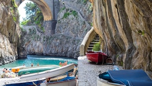 Una zona costera con barcos amarrados, un puente de piedra y una escalera que baja hacia el agua.