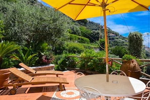 A terrace with a table and chairs, a yellow umbrella, and a view of a hillside.