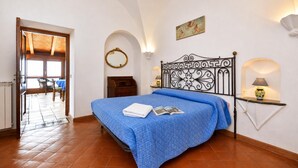 Un dormitorio con cama, mesita de noche, espejo en la pared y puerta que da a un balcón.