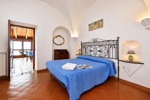 A bedroom with a bed, a bedside table, a wall-mounted mirror, and a door leading to a balcony.