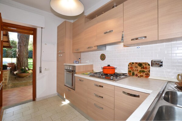 Een keuken met houten kastjes, een gasfornuis, een spoelbak en uitzicht op de omgeving.