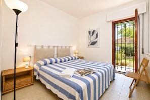Une chambre à coucher avec un lit, des lampes de chevet, une chaise, une fenêtre donnant sur un beau paysage et une porte.