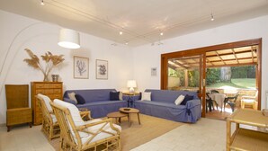 A living room with a blue sofa, wicker chairs, a small table, and a lamp. There is a wooden cabinet and a framed picture on the wall.