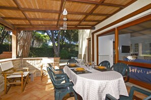Une terrasse extérieure avec une table dressée pour le repas, entourée de chaises, et offrant une vue sur l’extérieur.