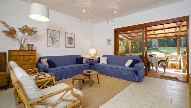 A living room with a blue sofa, a wicker chair, a small table, and a lamp. There is a wooden cabinet and a framed picture on the wall.