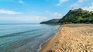 A beach with clear water, a sandy shore, and a building on a hill.