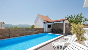 Une piscine sur le toit, agrémentée de chaises longues blanches, un bâtiment en pierre avec un toit en tuiles et une vue sur les montagnes lointaines.
