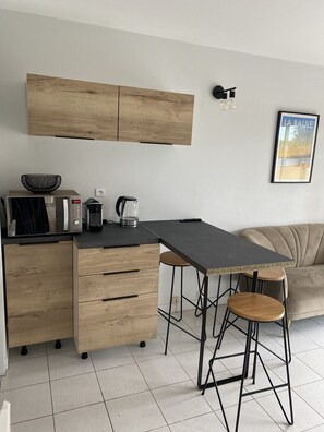 Une cuisine moderne avec des meubles en bois, un four à micro-ondes, une bouilloire et une machine à café. Le coin salon comprend un tabouret de bar et un canapé.