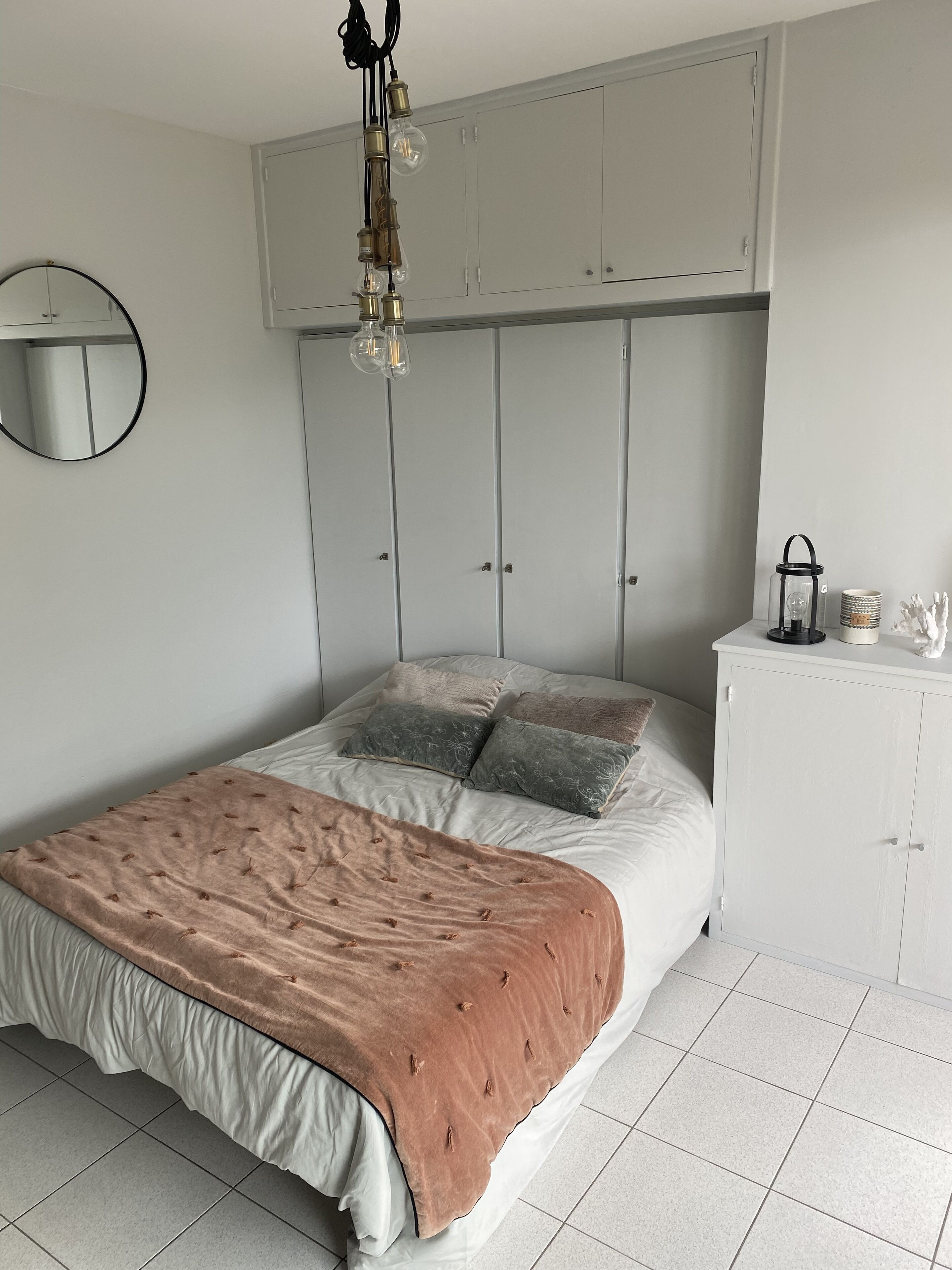 A bedroom with a bed, a wardrobe, a mirror, and a hanging light fixture.