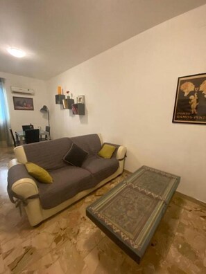 A living room with a sofa, a coffee table, and a wall-mounted shelf with decorative items.
