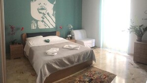 Ein Schlafzimmer mit einem Bett, einem Sessel, einem Nachttisch, einer Lampe und einer großen Wandmalerei.