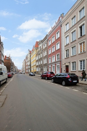 A street lined with colorful buildings, parked cars, and a clear sky.