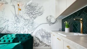 A modern kitchen with a green upholstered sofa, a wall with a floral mural, and a black tiled backsplash. - Elite Apartments Ogarna Prestige (Gdansk)