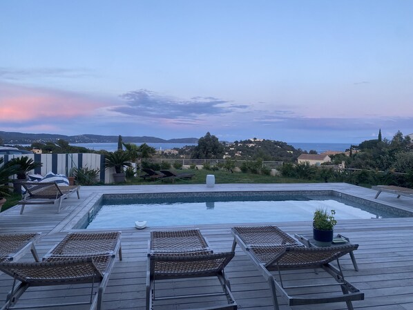 Un espace aménagé au bord de la piscine, avec des chaises longues et une vue sur la mer et les collines.