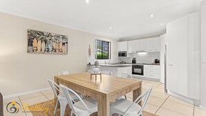 A modern kitchen with white cabinets, a wooden dining table, and a painting on the wall.