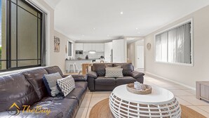 A modern living room with a leather sofa, a round coffee table, and a dining area in the background.