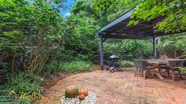Un patio con pérgola, mobiliario exterior y una parrilla.
