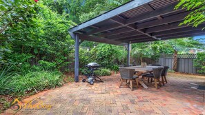 Un patio con una parrilla, mobiliario exterior y una pérgola.