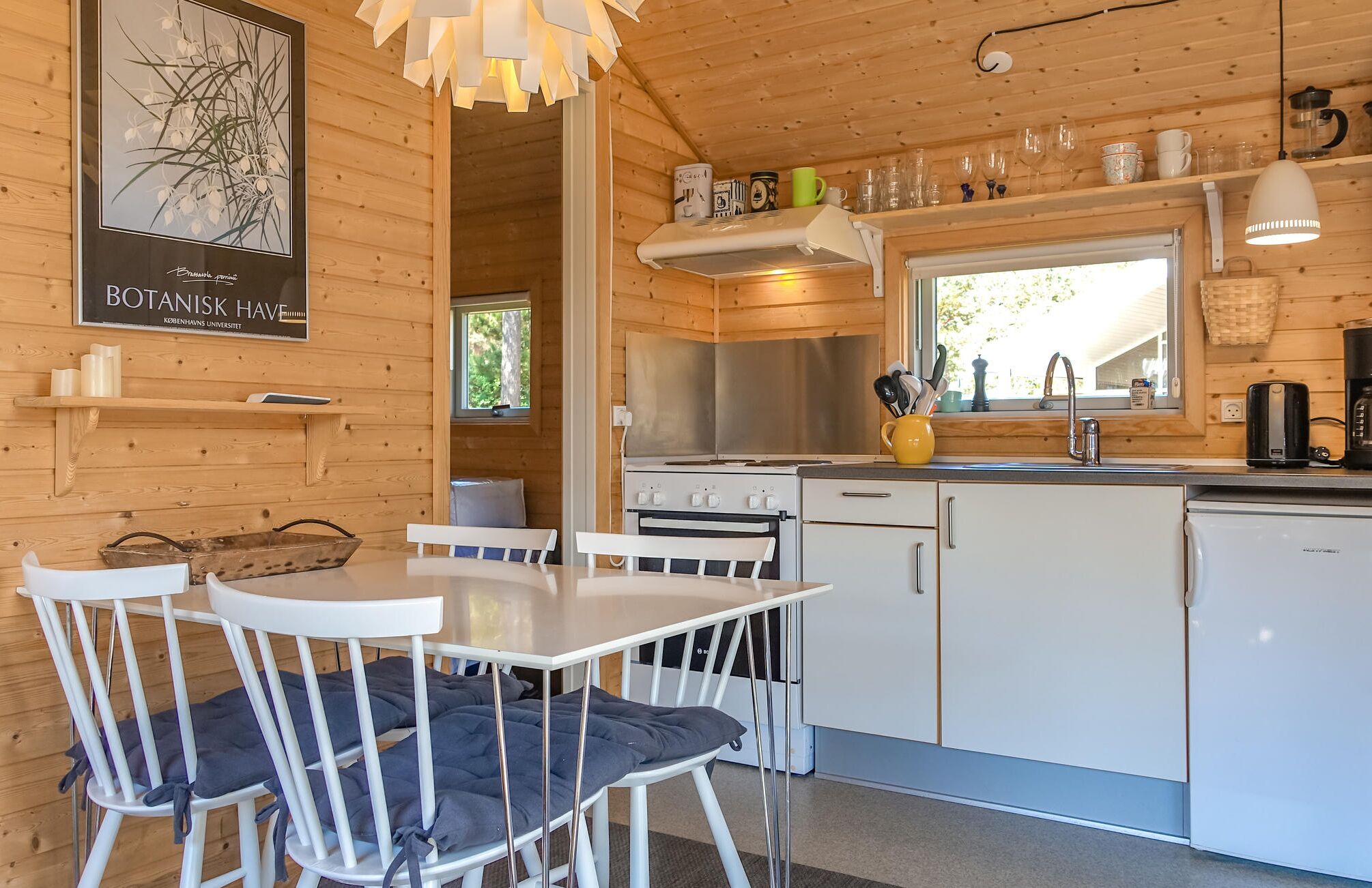 A wooden cabin interior with a dining area, kitchen, and a poster on the wall.