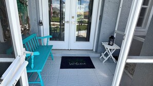 A covered porch with a bench, a welcome mat, and a small table with a lantern. - Vacation in Paradise on the Canal w/Heated Pool, minutes to Beach, Dog Friendly! (Rotonda West)