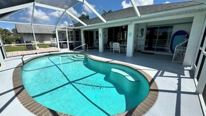 A covered swimming pool with a brick edge, a patio area with outdoor furniture, and a building with large windows and a covered entrance. - Vacation in Paradise on the Canal w/Heated Pool, minutes to Beach, Dog Friendly! (Rotonda West)