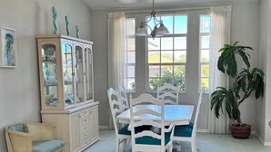 A dining room with a white table and chairs, a wooden cabinet with glass doors, a wicker chair, and a potted plant. - Vacation in Paradise on the Canal w/Heated Pool, minutes to Beach, Dog Friendly! (Rotonda West)