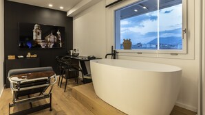 A modern bathroom with a large bathtub, a vanity with a mirror, and a window with a view of a cityscape. - MICELI EXCLUSIVE SUITE (Palermo)