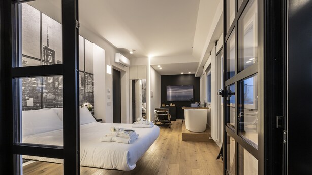 A modern hotel room with a large bed, a desk, and a view of the cityscape through floor-to-ceiling windows. - MICELI EXCLUSIVE SUITE (Palermo)