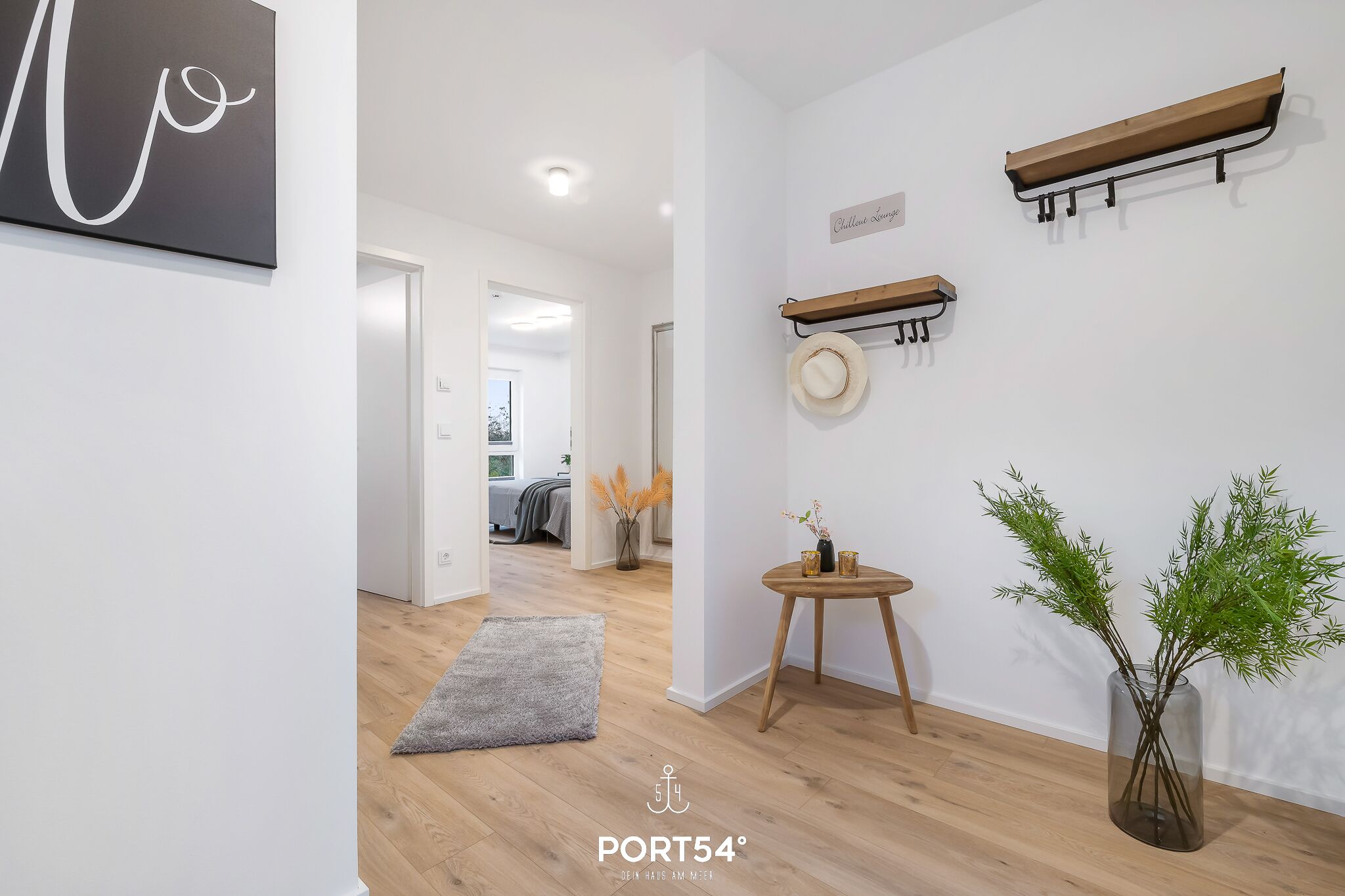 A modern interior with a hallway leading to a bedroom, a wall-mounted hat rack, a small wooden table with a vase, and a plant.