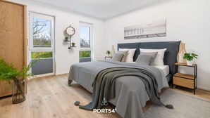 Et moderne soveværelse med en stor seng, et natbord med en plante, et vindue med udsigt og en lampe i loftet.