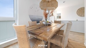 En spiseplads med et træbord, fletstole, en hængende lampe i flet og et vægur.