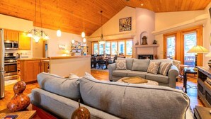 A spacious living area with a large gray sofa, wooden ceiling, and a kitchen in the background.