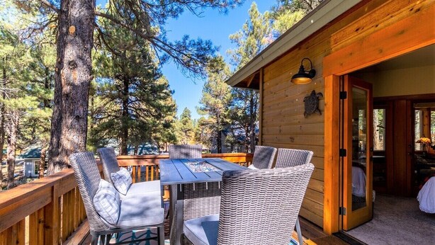 A wooden cabin with a deck, wicker furniture, and a glass table.