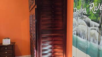 Una stanza con una porta in legno, pavimento piastrellato, un comò e un quadro che raffigura un fiume.