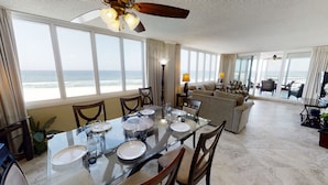 A spacious living area with a large glass dining table, comfortable seating, and a view of the ocean.