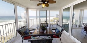 Un balcón con puerta de vidrio que da a una vista de la playa, muebles de mimbre y un ventilador de techo.