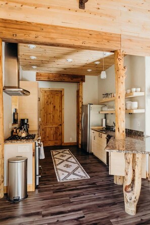 A modern kitchen with wooden beams, a central island, stainless steel appliances, and a patterned rug.