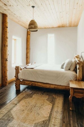 Une chambre à coucher rustique avec un lit en bois, un luminaire suspendu et une grande fenêtre.