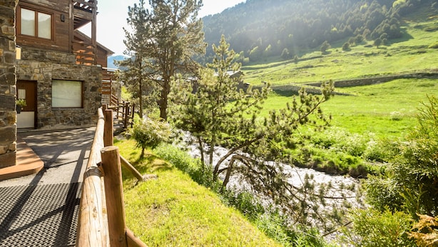 Un chalet rustique aux murs de pierre et aux balcons en bois, offrant une vue sur une vallée verdoyante et une rivière.